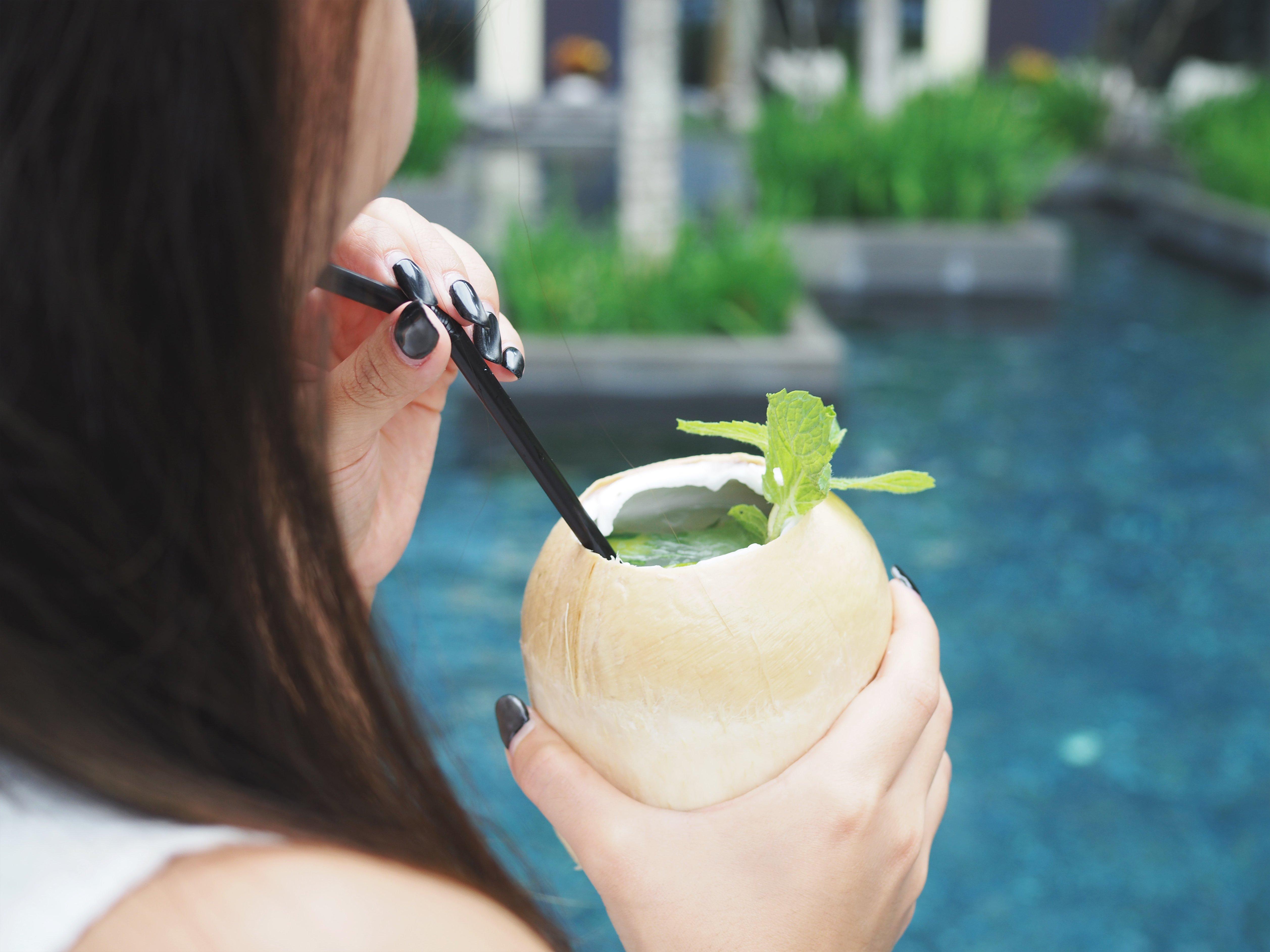 Crowne Plaza Changi Airport By Ihg Сінгапур Екстер'єр фото The photo features a person holding a coconut drink with a straw. The drink is garnished with a sprig of mint. The background shows a blue pool, suggesting a tropical or relaxing setting. The focus is on the drink and the person's hand.