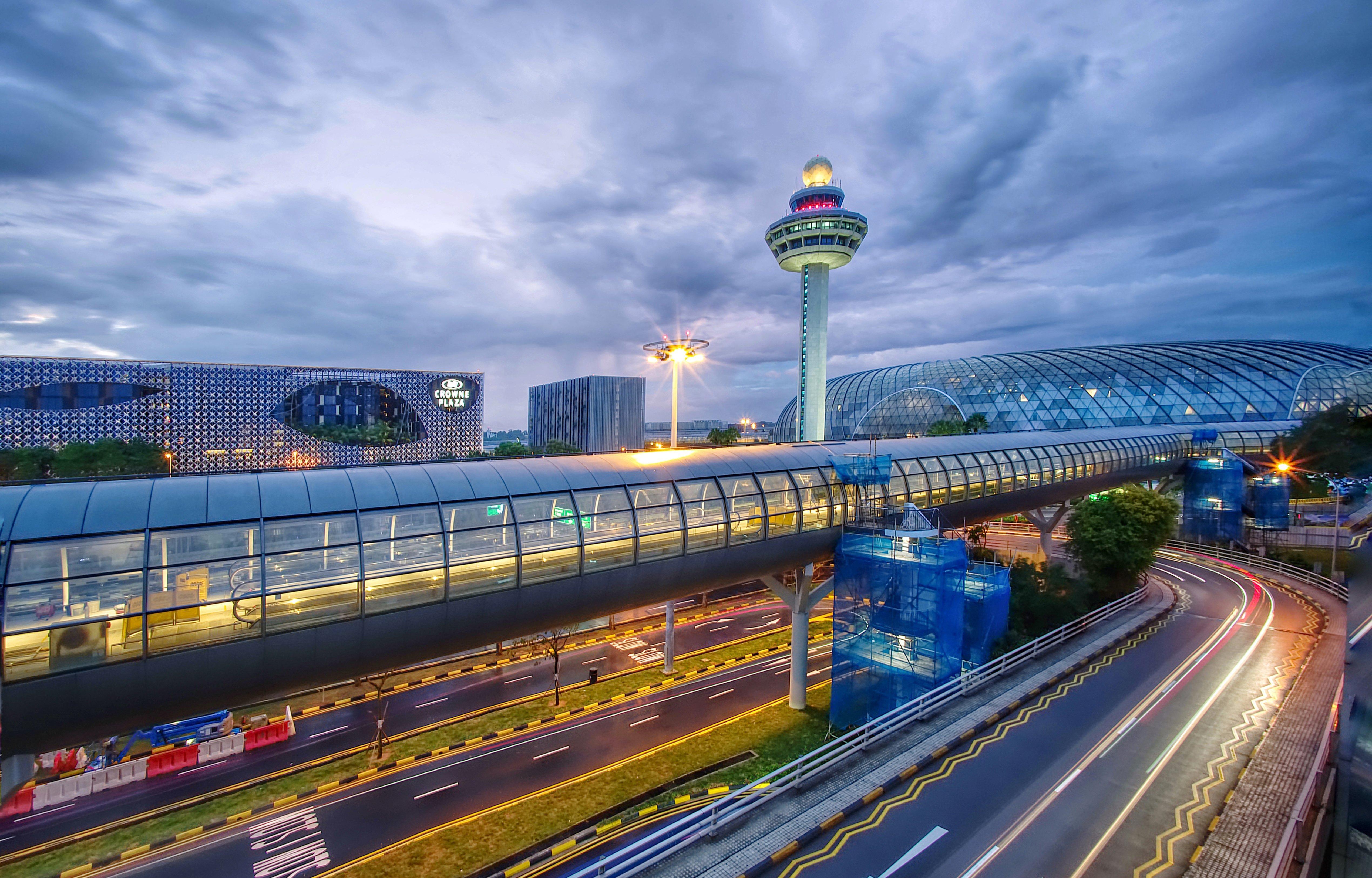 Crowne Plaza Changi Airport By Ihg Сінгапур Екстер'єр фото The photo depicts an airport scene, likely featuring a modern terminal structure with a distinctive, futuristic design. In the foreground, there is a pedestrian bridge or walkway, along with roads leading to the terminal. A control tower can be seen 