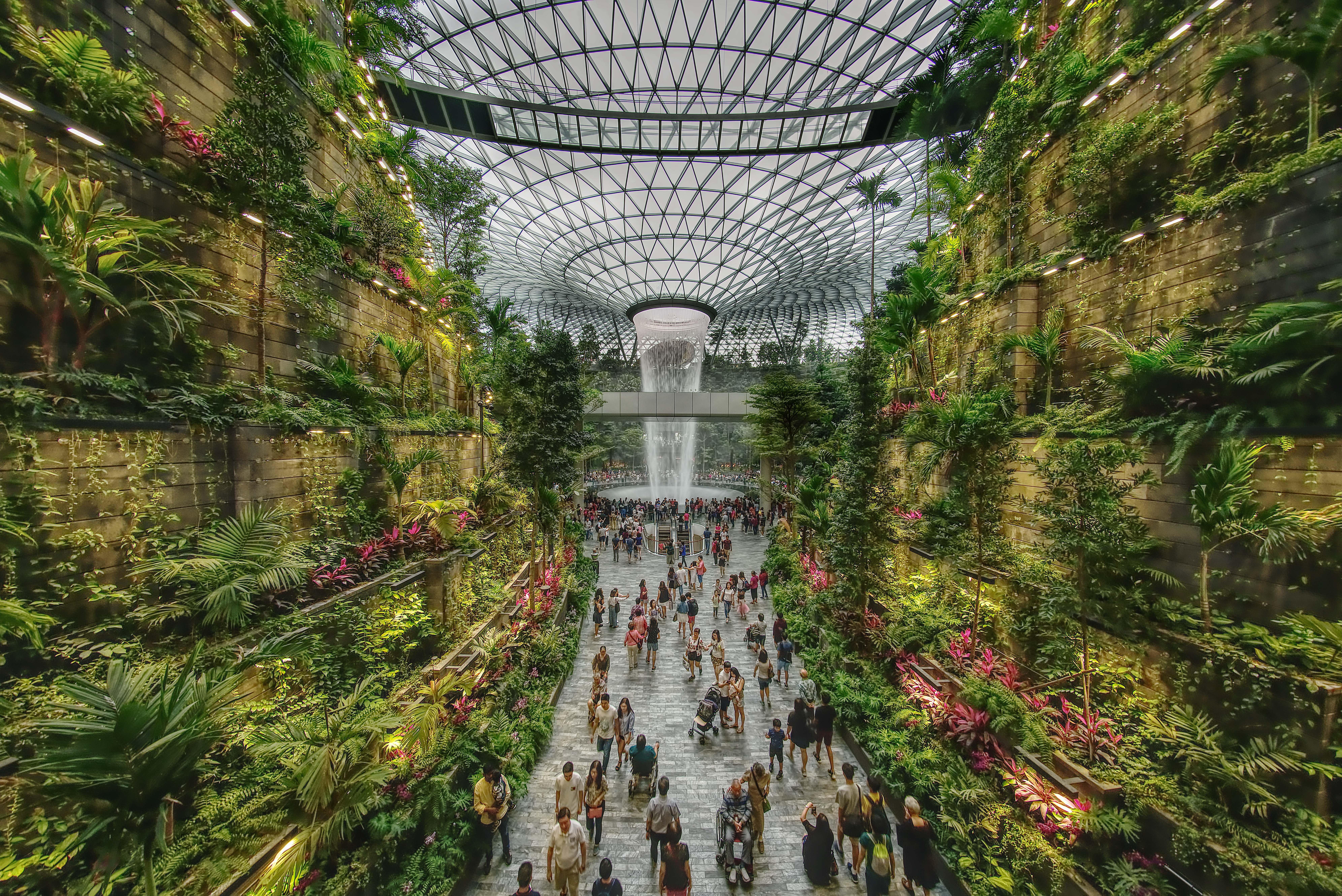 Crowne Plaza Changi Airport By Ihg Сінгапур Екстер'єр фото The photo depicts a vibrant indoor garden space, characterized by lush greenery and a towering waterfall at its center. The setting features vertical gardens on stone walls, filled with various plants and flowers. People can be seen walking along the