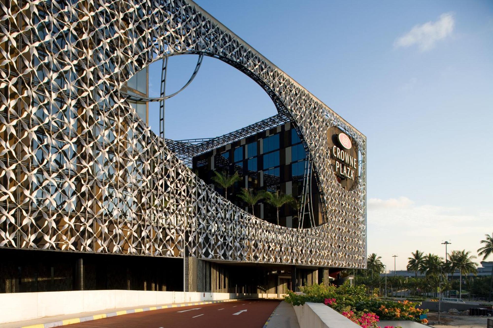 Crowne Plaza Changi Airport By Ihg Сінгапур Екстер'єр фото The photo features a modern building with a unique architectural design. The facade consists of a complex lattice structure that creates a visual pattern, including a large circular cutout. The building appears to be multi-story, with large glass win