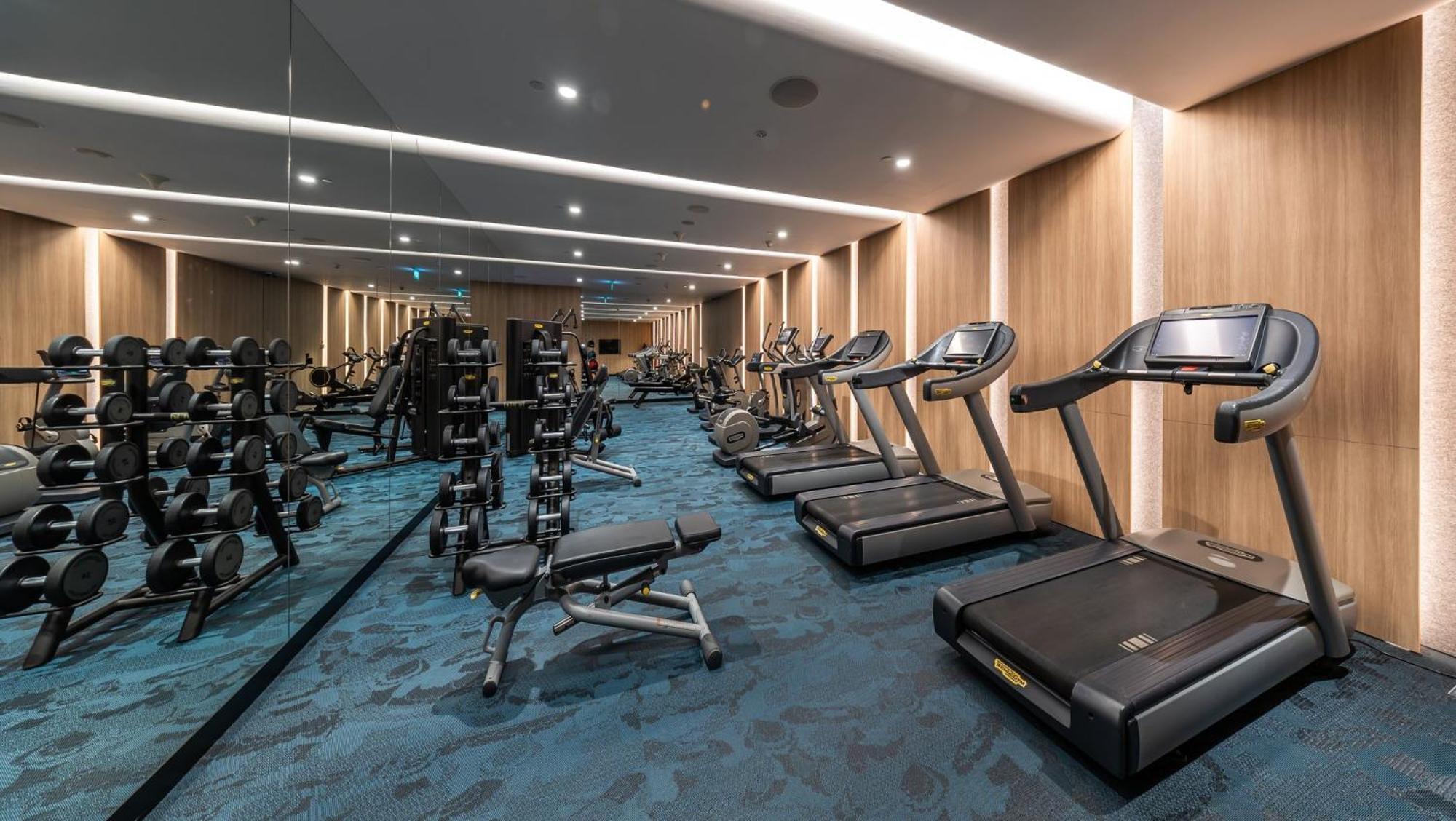 Crowne Plaza Changi Airport By Ihg Сінгапур Екстер'єр фото The photo shows a well-equipped gym or fitness room. On one side, there are several weightlifting benches along with dumbbells arranged on racks. On the other side, there are multiple treadmills lined up, suggesting a space designed for both strength