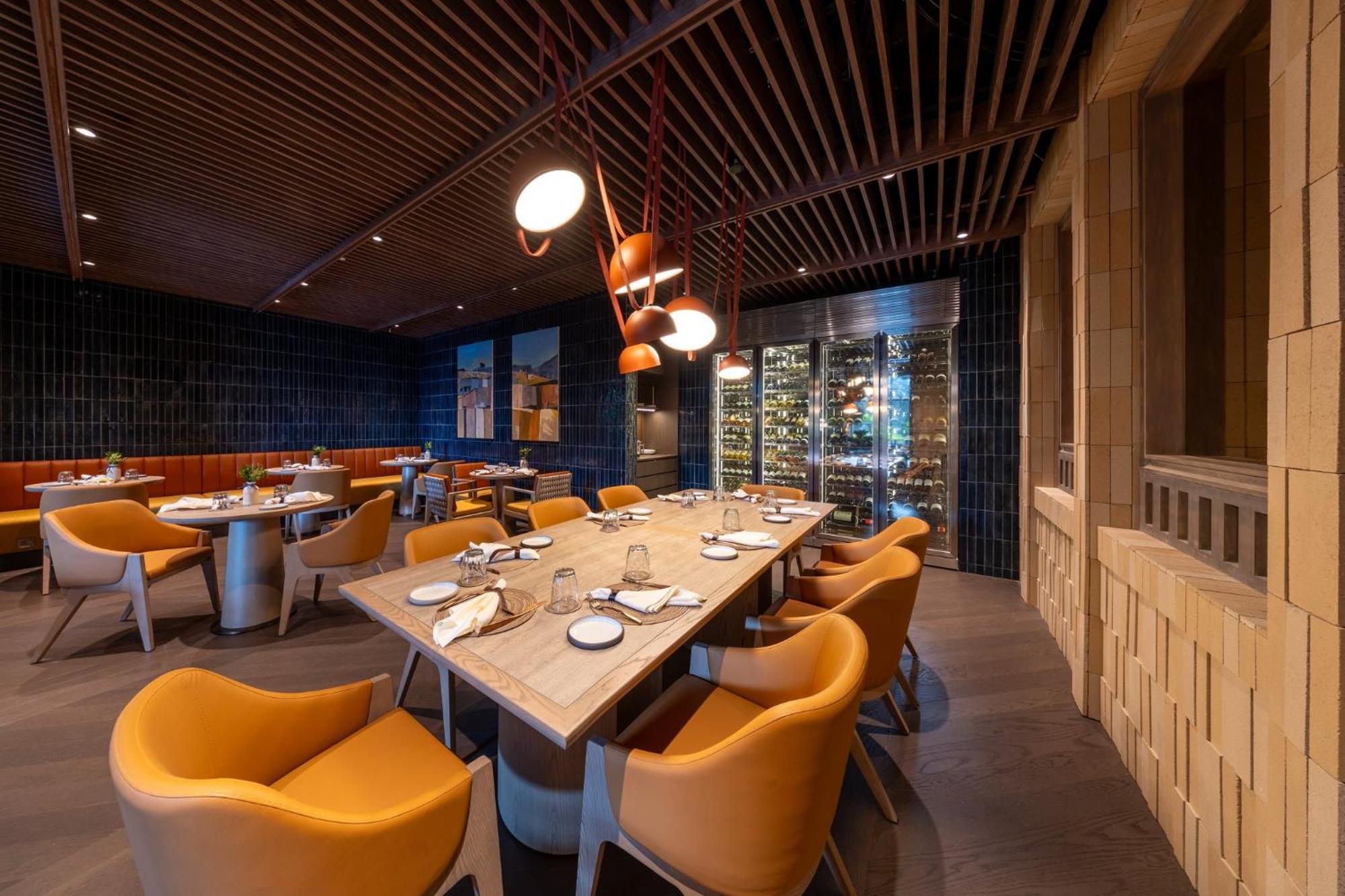 Crowne Plaza Changi Airport By Ihg Сінгапур Екстер'єр фото The photo shows an elegant restaurant interior featuring a modern design. In the center, there is a large wooden table set for dining, with white plates and utensils arranged neatly. Surrounding the table are vibrant orange chairs that provide a cozy