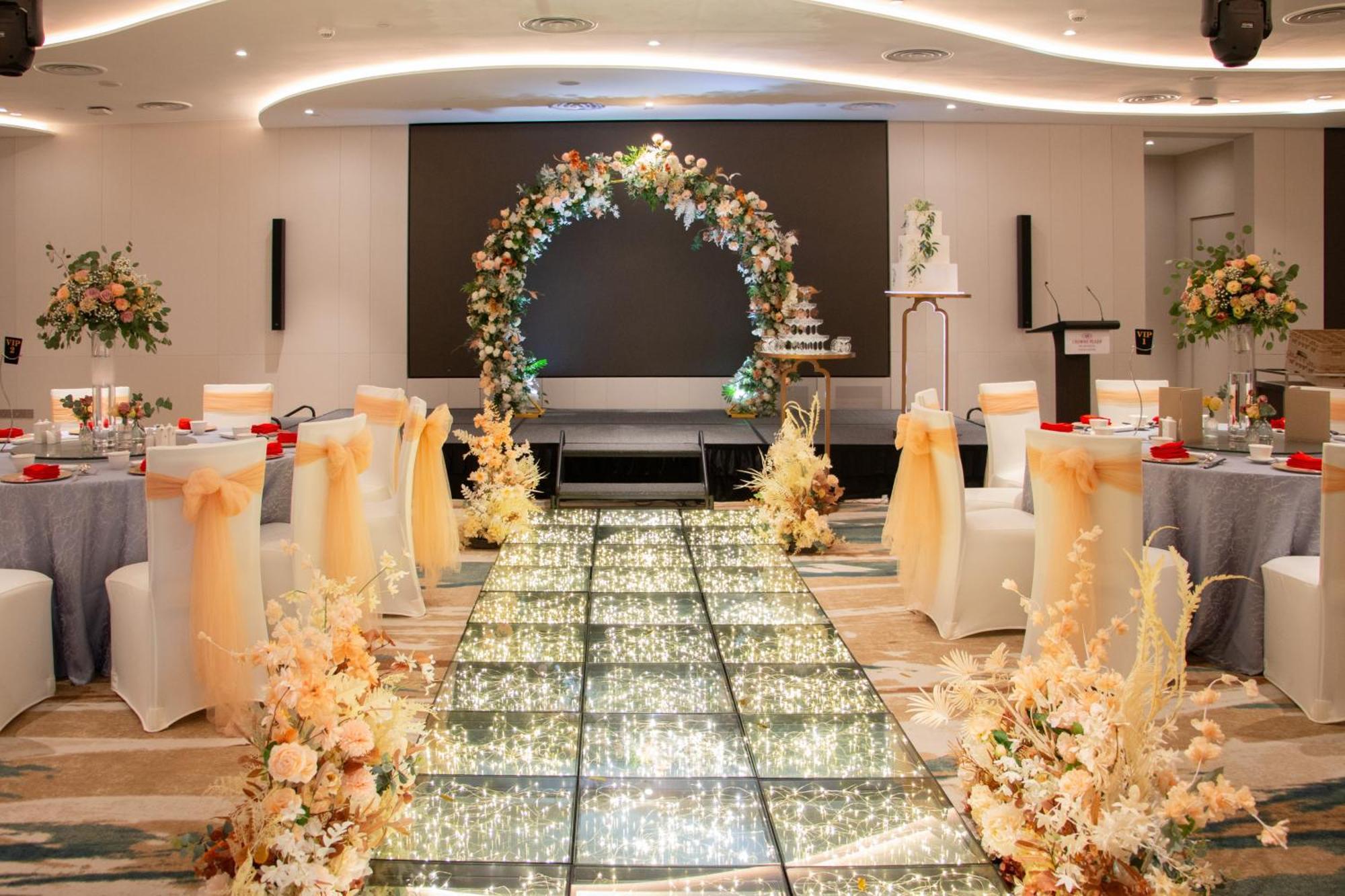 Crowne Plaza Changi Airport By Ihg Сінгапур Екстер'єр фото The image depicts an elegantly decorated event space, likely for a wedding or formal occasion. In the center, there is a flower-adorned archway in warm colors, creating a focal point. A sparkling, illuminated pathway leads towards the arch, bordered 