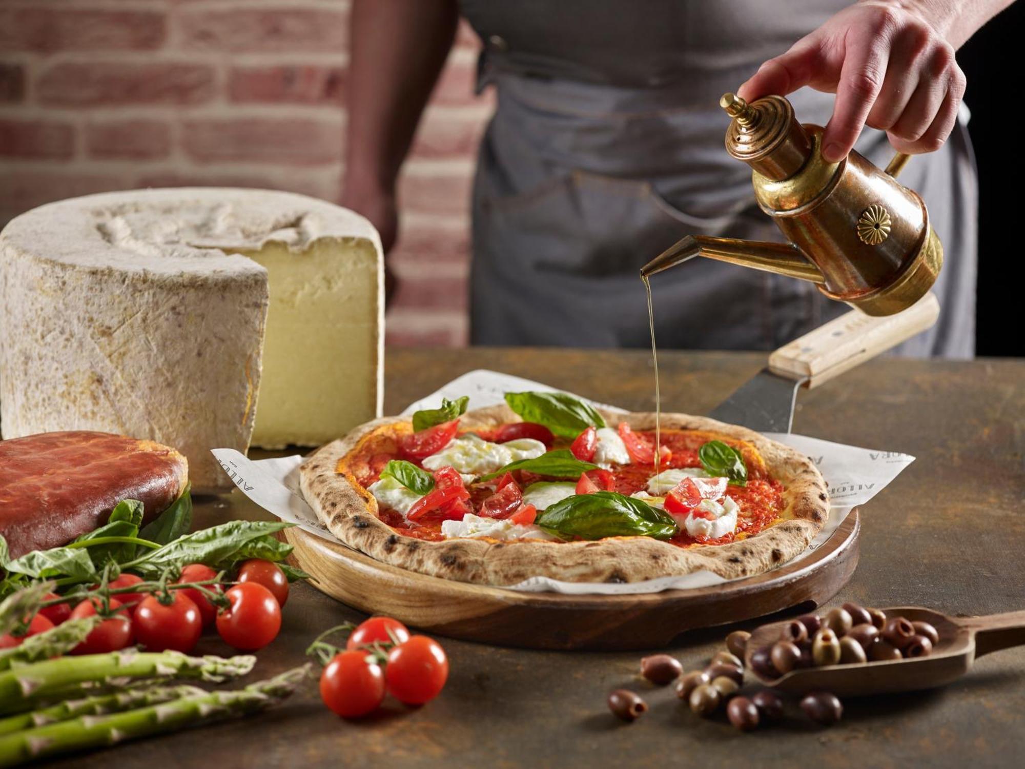 Crowne Plaza Changi Airport By Ihg Сінгапур Екстер'єр фото The photo features a freshly made pizza being drizzled with oil. The pizza is topped with ingredients such as fresh basil and tomatoes, and has a golden, crispy crust. In the background, there is a block of cheese and a piece of ham. Surrounding the 