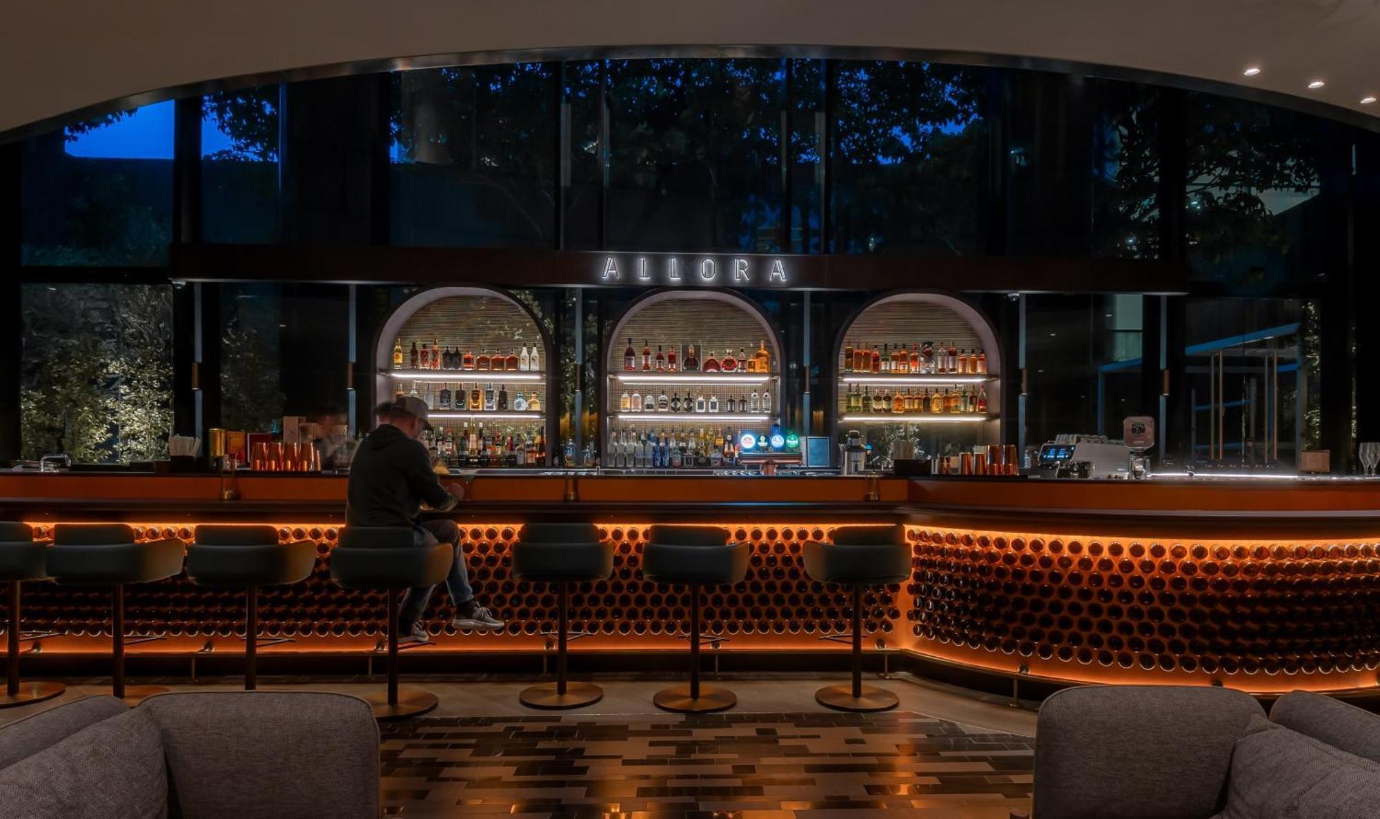 Crowne Plaza Changi Airport By Ihg Сінгапур Екстер'єр фото The photo shows a bar area with a modern and stylish design. In the center, there is a well-lit bar counter featuring a variety of alcoholic beverages displayed on shelves behind it. The bar has a sleek, contemporary look with circular light fixtures