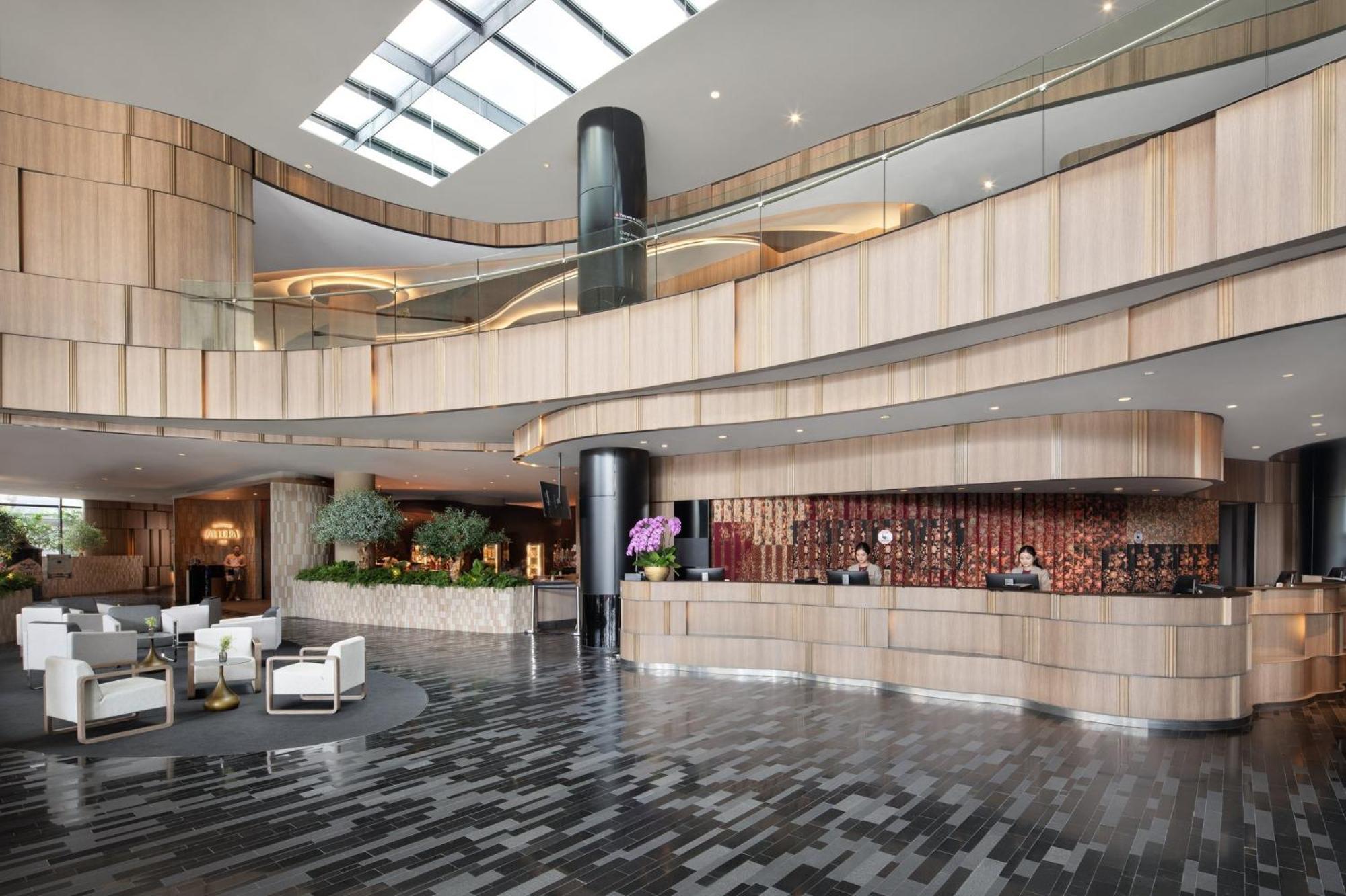 Crowne Plaza Changi Airport By Ihg Сінгапур Екстер'єр фото The photo shows a modern hotel lobby with a sleek and stylish design. The reception area features a curved wooden counter, with staff members attending to guests. The interior design includes a mix of wood and stone materials, creating a warm and inv