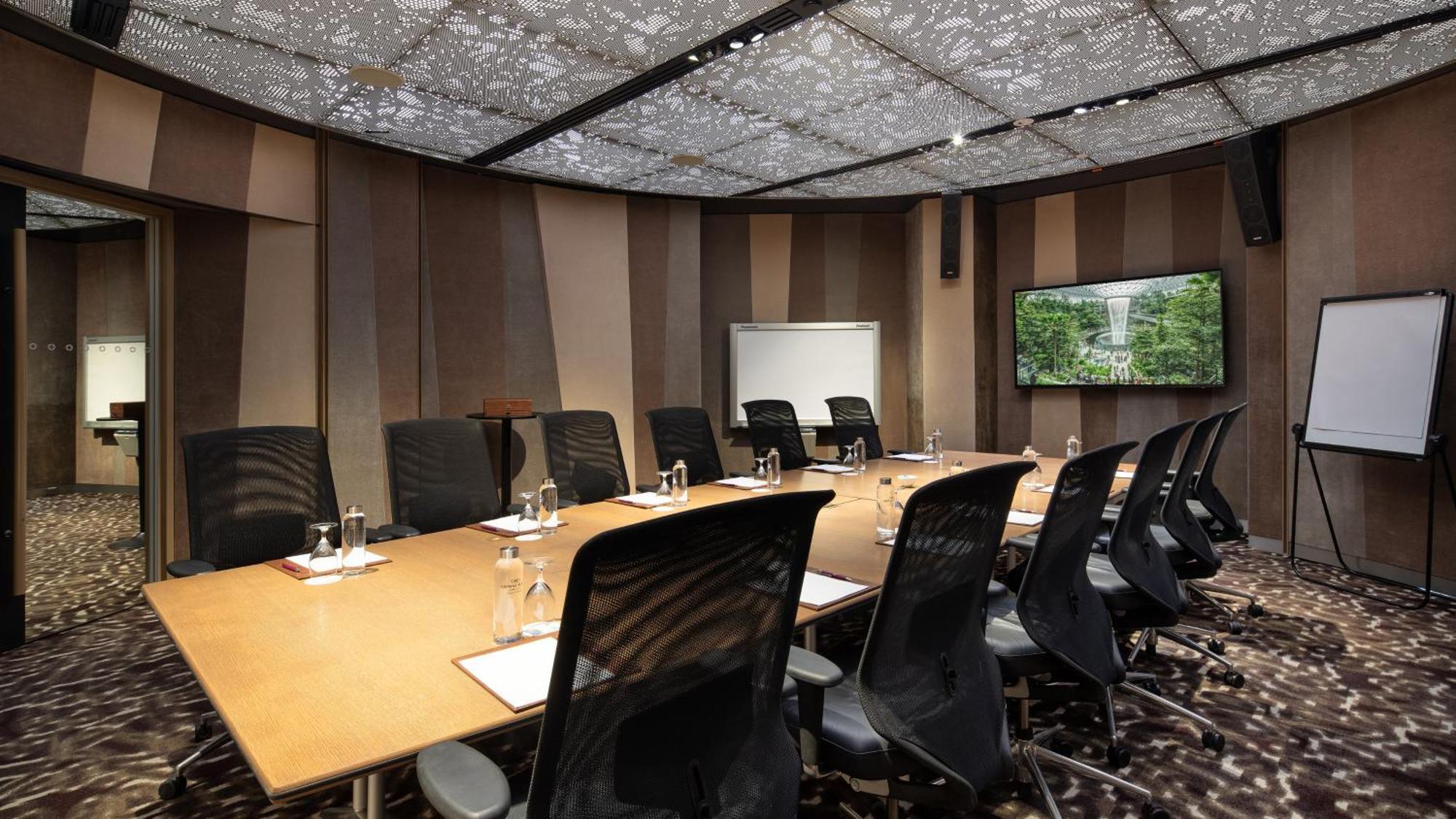 Crowne Plaza Changi Airport By Ihg Сінгапур Екстер'єр фото The image shows a modern conference room. It features a large rectangular table surrounded by black ergonomic chairs. On the table, there are glasses of water, notepads, and pens. The walls have a sleek design with alternating patterns in neutral col